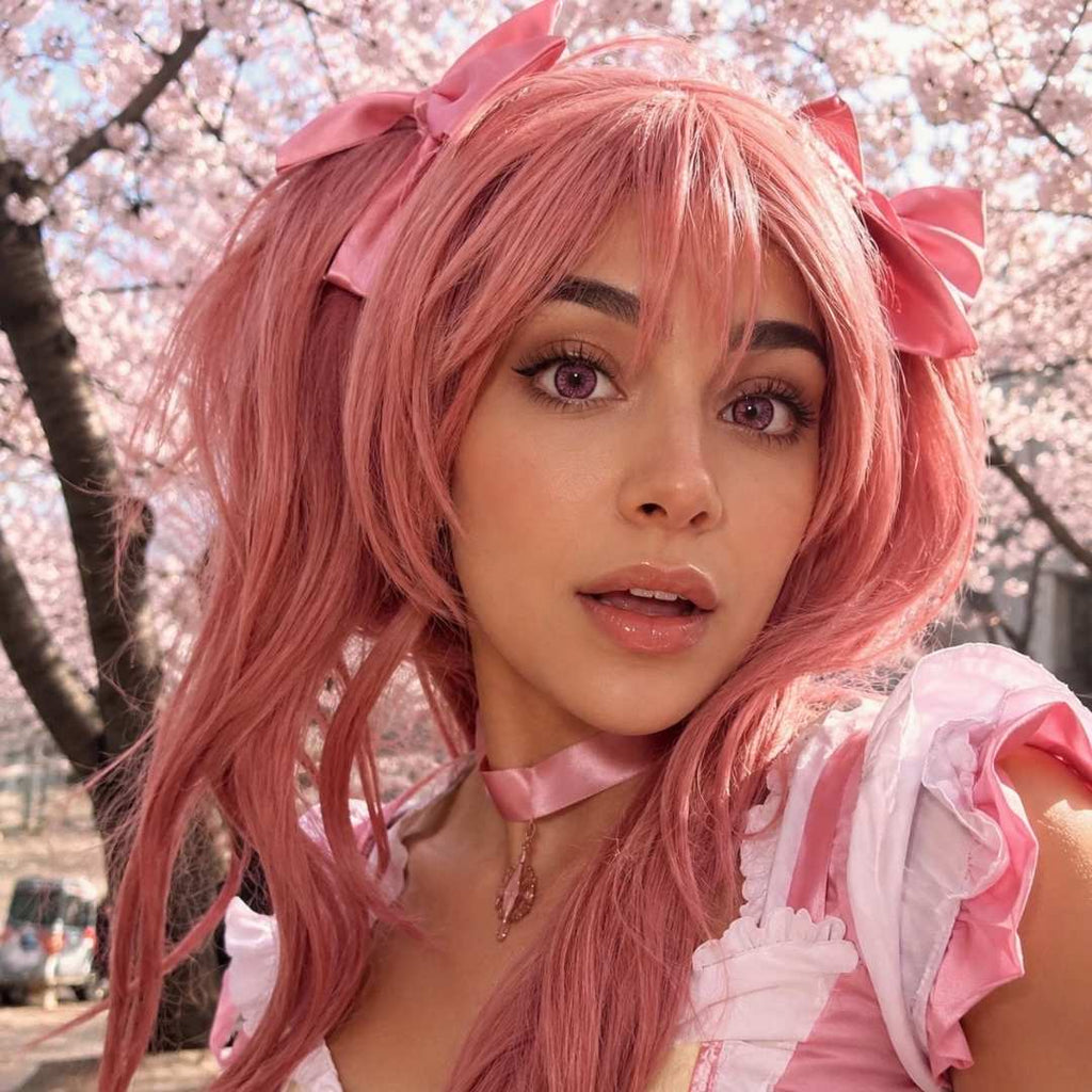 Cosplayer dressed as a pink cat girl with bows and a heart choker, surrounded by flowers.