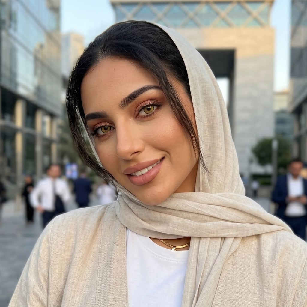 A woman with a headscarf and white shirt gazes thoughtfully, embodying grace and elegance.