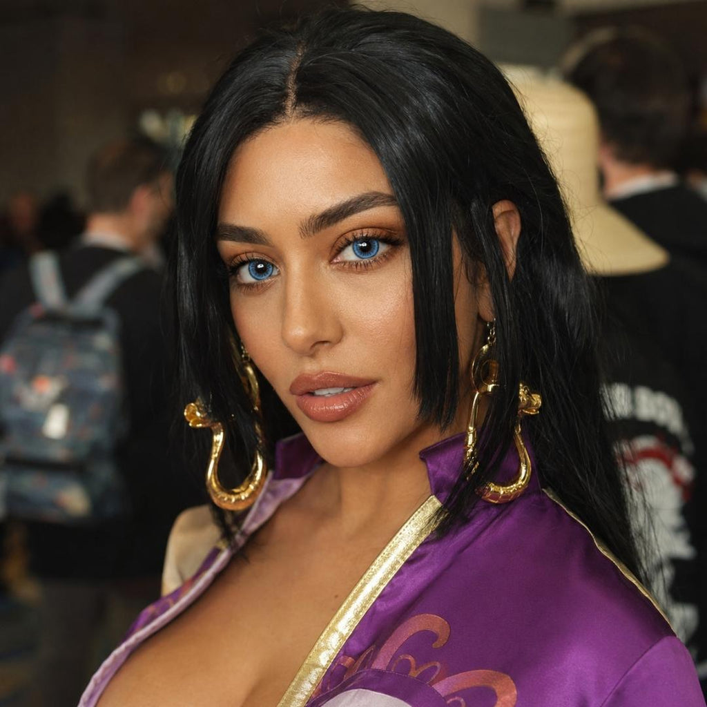 Portrait of a cosplayer with sleek black hair and oversized gold earrings wearing a purple costume at a convention. Her dramatic blue lens look contrasts with the rich colors of the outfit and blurred crowd behind her.