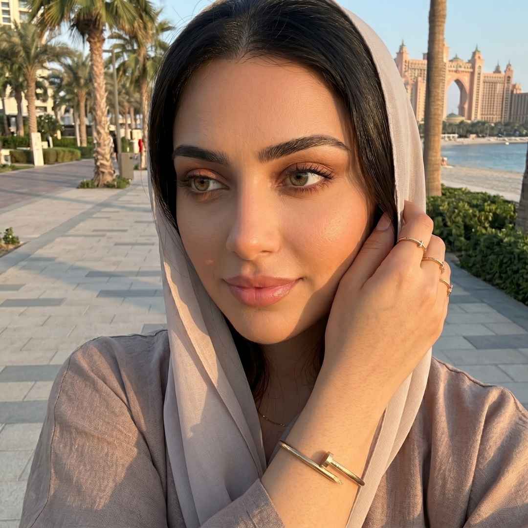 Woman adjusting her headscarf with a scenic background of palm trees and buildings.
