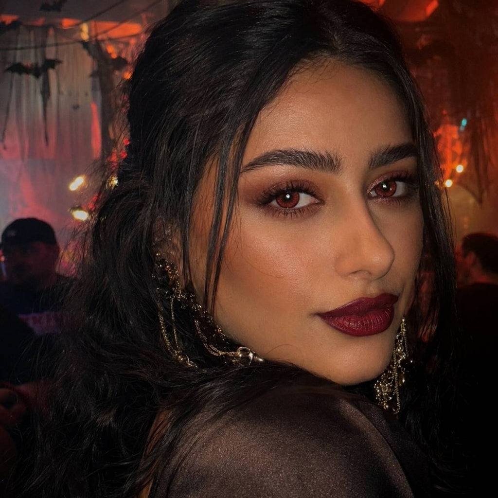 Close-up of a woman with dark hair, red contact lens and red lipstick in an indoor setting with blurred background