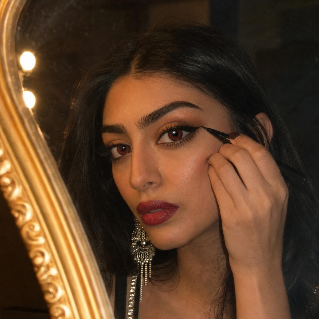 Woman wearing reem adult red contact lenses applying eyeliner in front of a mirror with a decorative frame.
