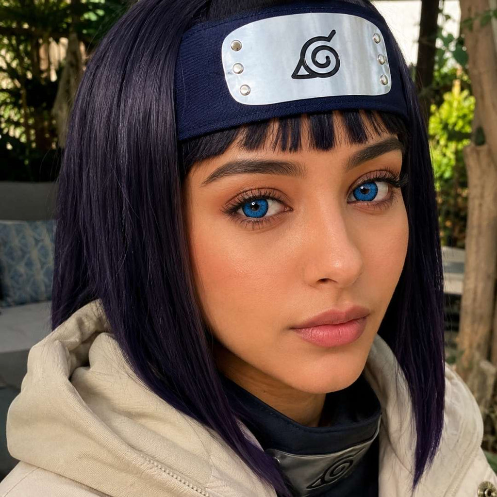 Lady cosplay as Hinata Hyuga wearing a headband with a symbol, outdoors with greenery in the background