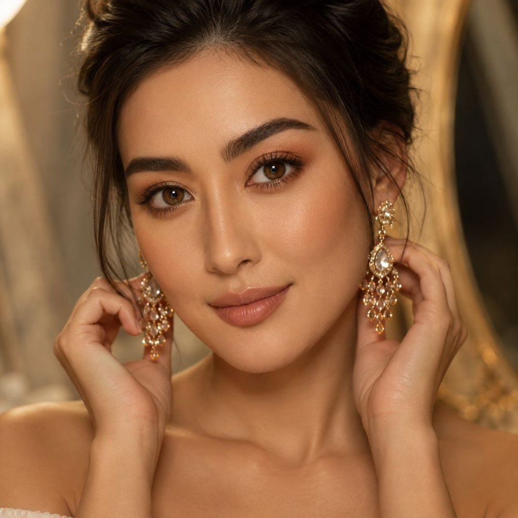 A glamorous woman putting on dangling diamond earrings, showcasing wide-eye brown contact lenses and a soft bridal makeup look.