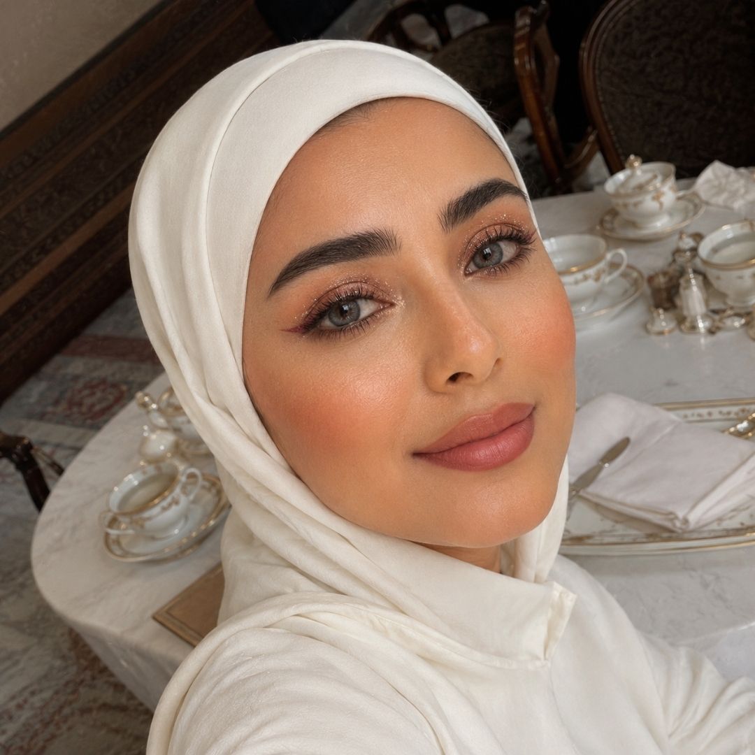 A woman in a white hijab sits at a table, her striking coco gray contact lenses enhancing her thoughtful expression.