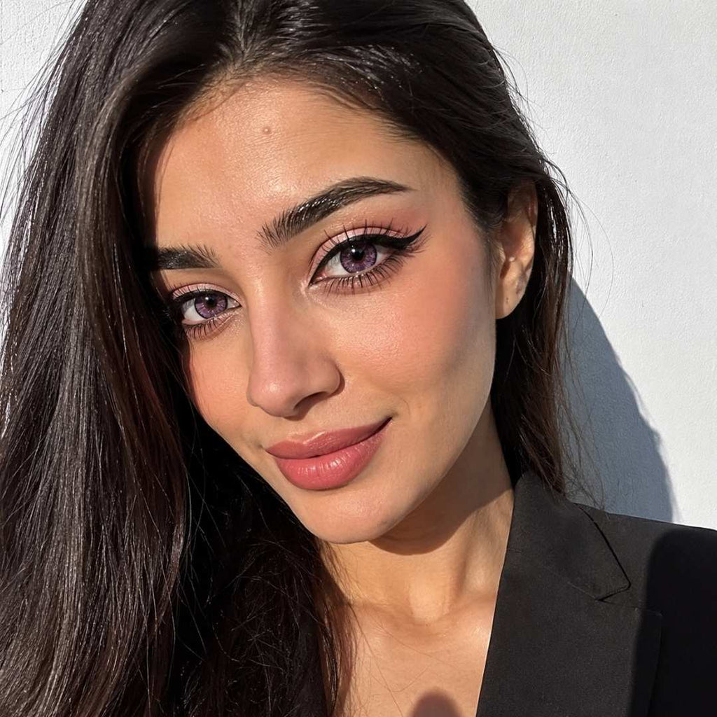 Sunlit beauty portrait with long dark hair, soft glam makeup, and pink contact lenses that create a subtle violet pink effect. Bright natural light highlights how the lenses remain visible on dark eyes while maintaining a natural appearance.