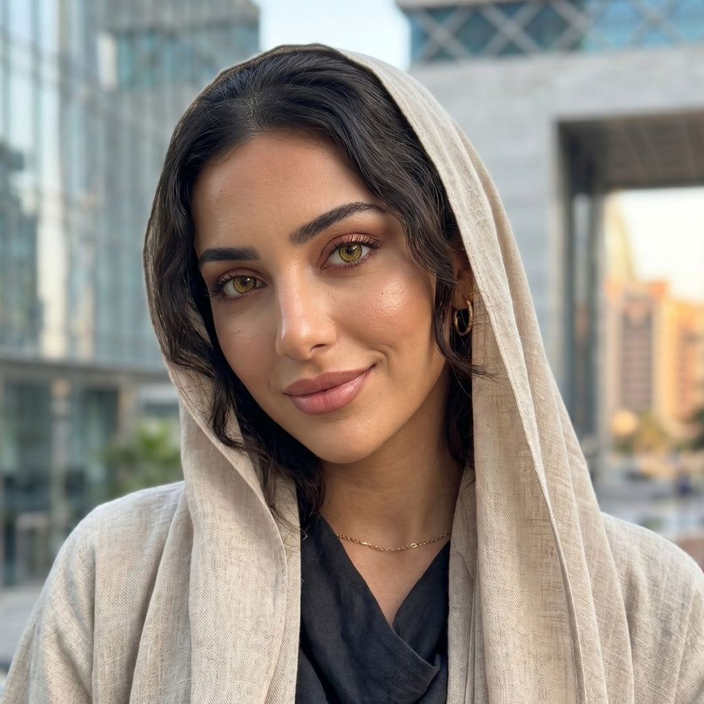 A woman with dolly brown eyes wearing a beige shawl over a black top, smiling softly at the camera.