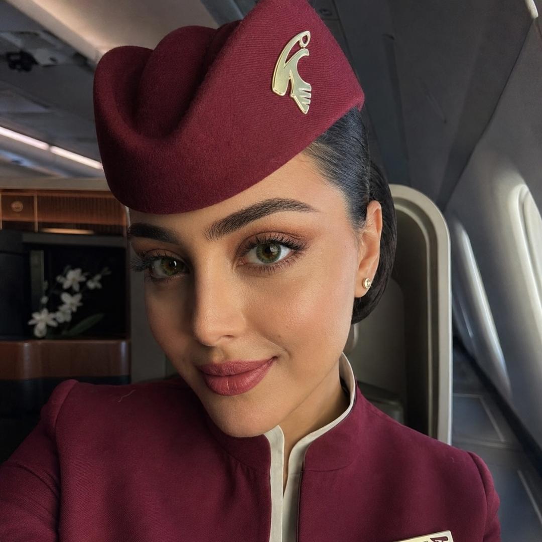 Subtle green colored contacts creating a natural eye look in airline uniform Airline stewardess wearing a maroon uniform with a logo in an airplane cabin.