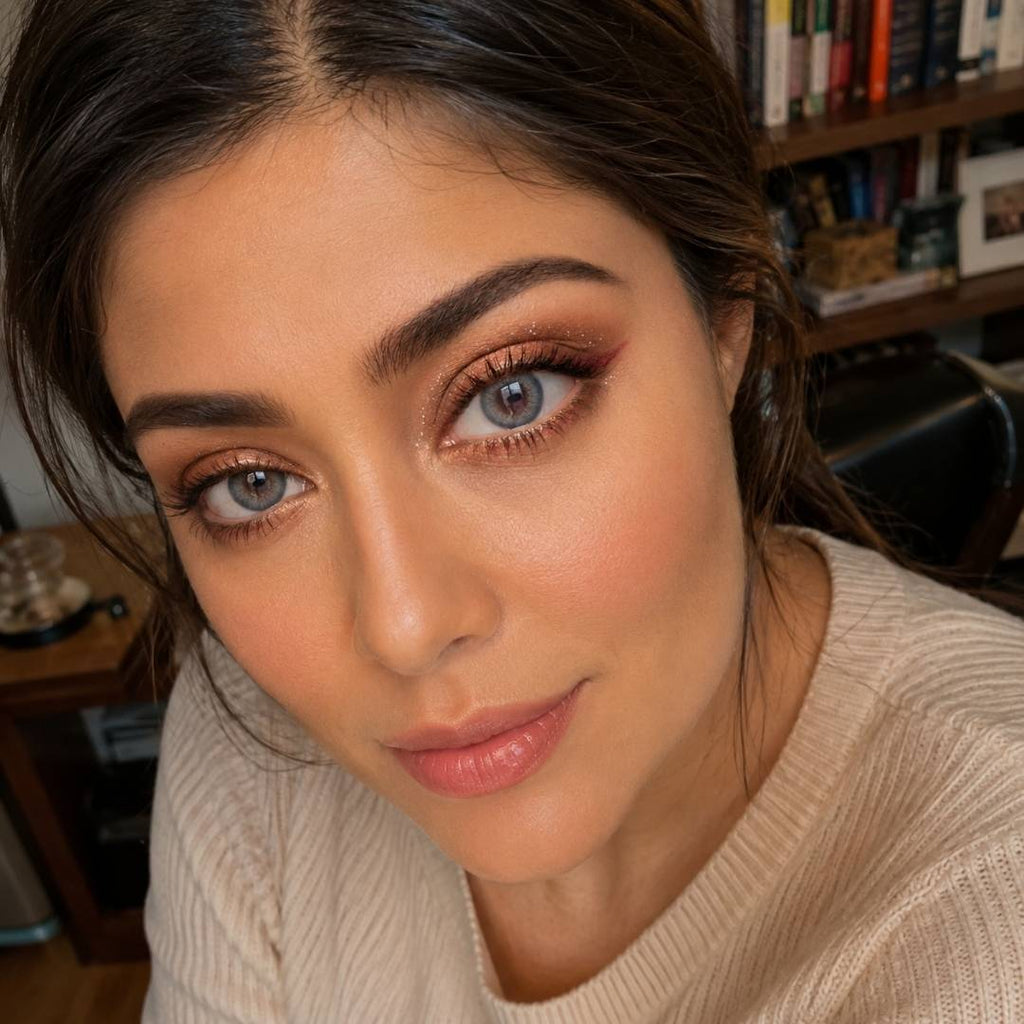 A woman with brown eyes wearing a white sweater and coco gray contact lenses, smiling softly at the camera.