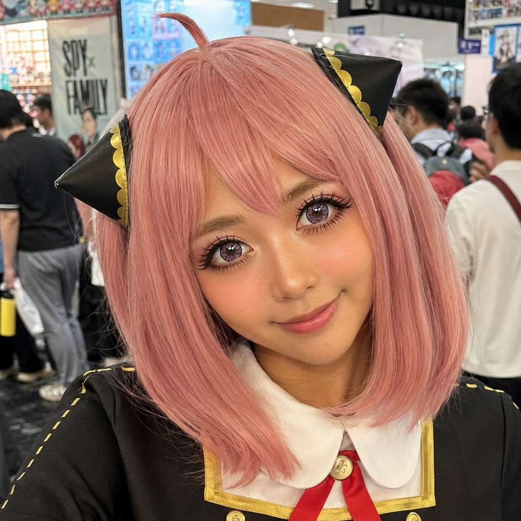 Convention cosplay portrait featuring a short pink wig, black and gold costume details, and pink cosplay contacts. The large doll like eyes and playful styling create a character inspired appearance.