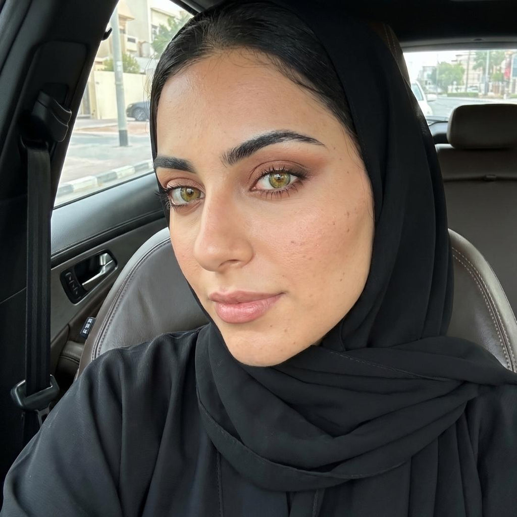 Woman wearing olive contact lens wearing a black hijab sitting inside a car.