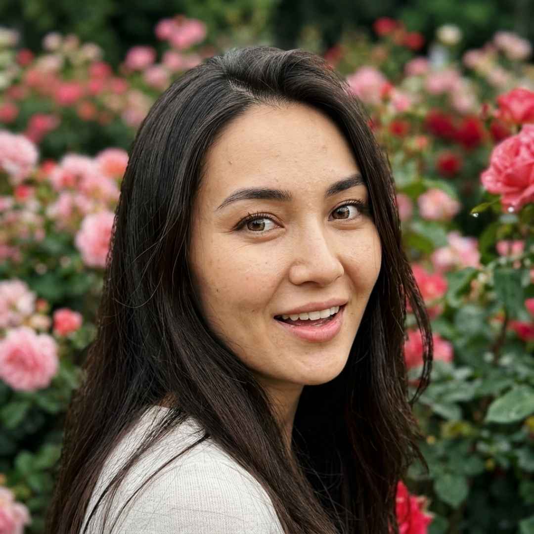 Woman with long dark hair smiling in front of pink flowers